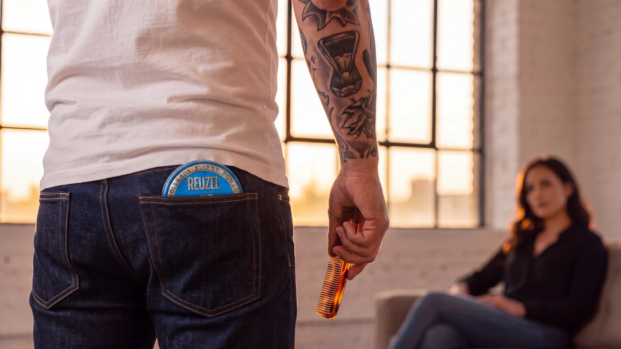 Reuzel grooming products styled in a bright widescreen lifestyle scene, with a model in a white shirt beside a window